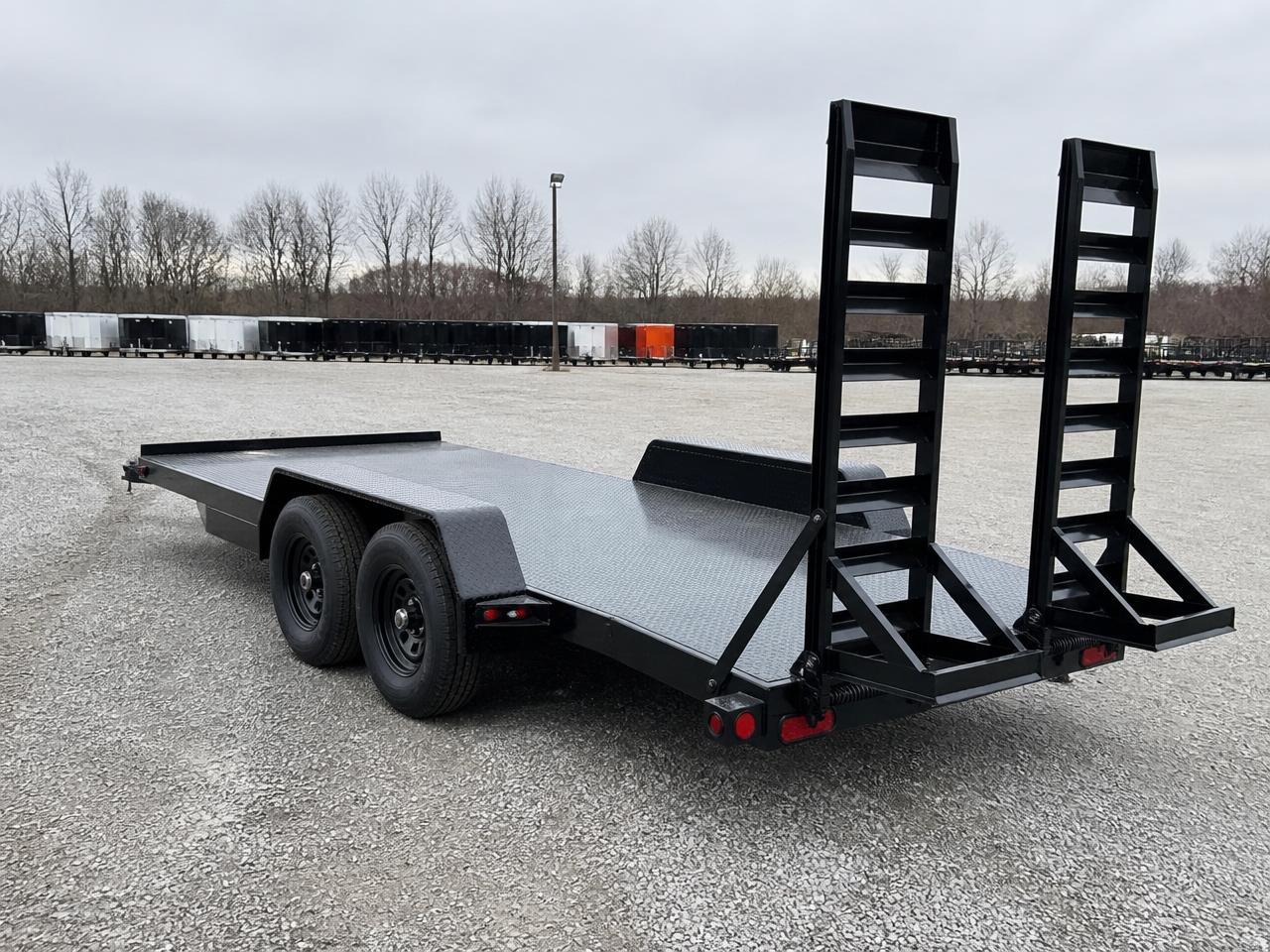 Black steel deck-over equipment trailer with fold-up rear ramps parked on a gravel lot